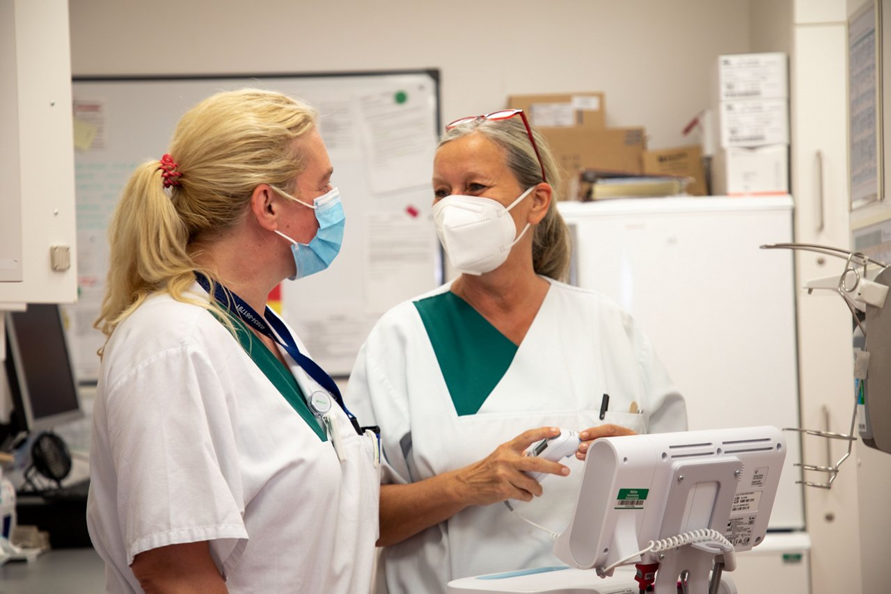 Schwestern stehen vor einem Monitor und sprechen miteinander.