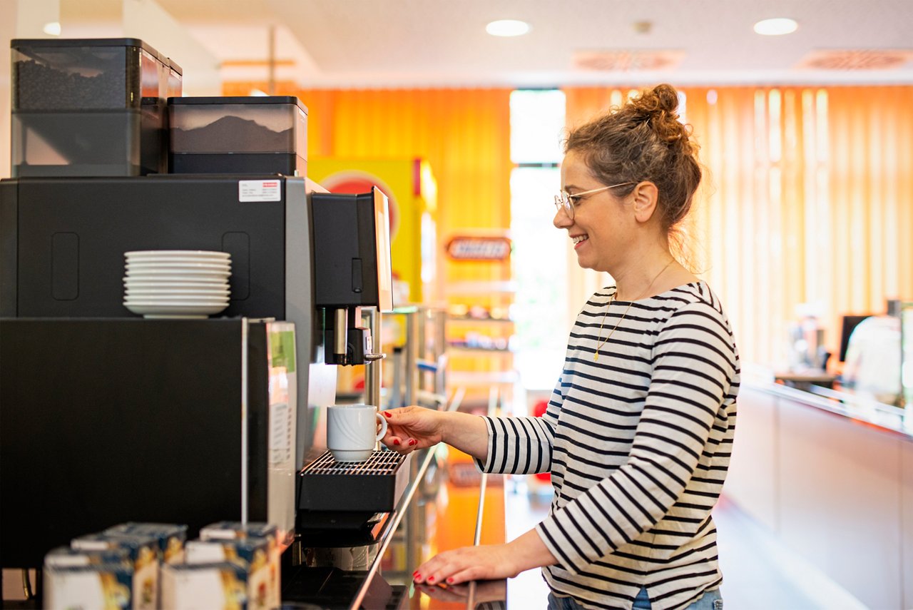 Besucherin in der Cafeteria in Huels zieht sich einen Kaffee am Automaten 