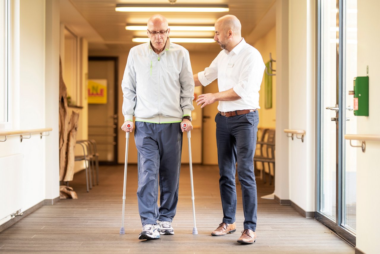 Arzt trainiert mit Patient nach dem Gelenkersatz auf Krücken zu gehen