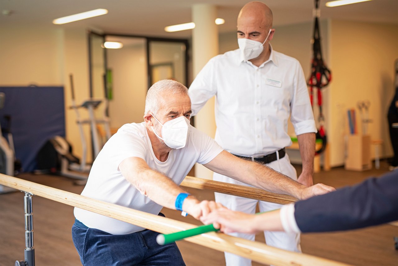 Patient mit Arzt und Physiotherapie bei Übungen an Turnstangen