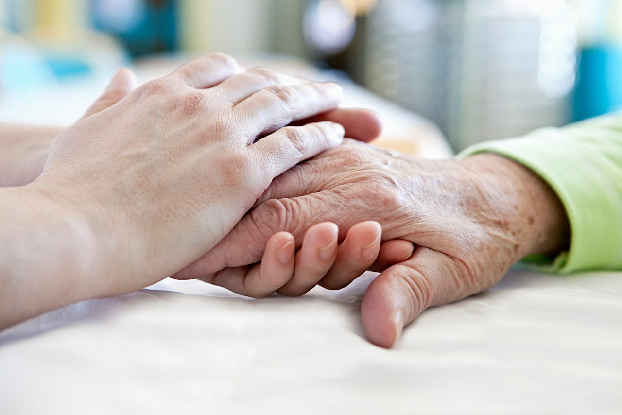 Pflegerin hält Hände einer Patientin