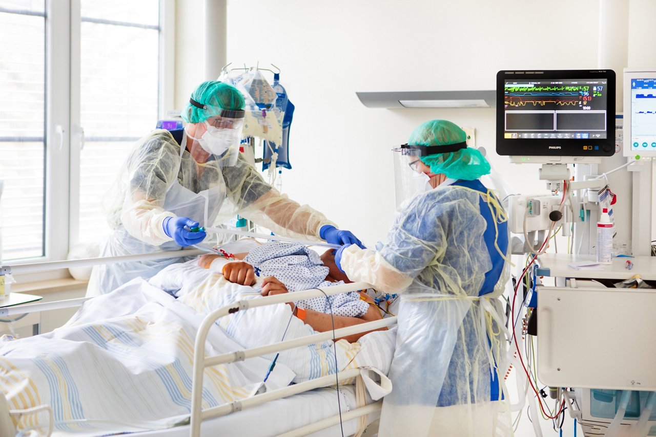 Zwei Pflegekräfte in Corona-Schutzkleidung  während pflegerischer und medizinischer Maßnahmen am Patienten 