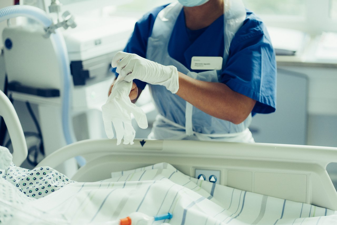 Pflegekraft zieht sich Handschuhe am Krankenbett über