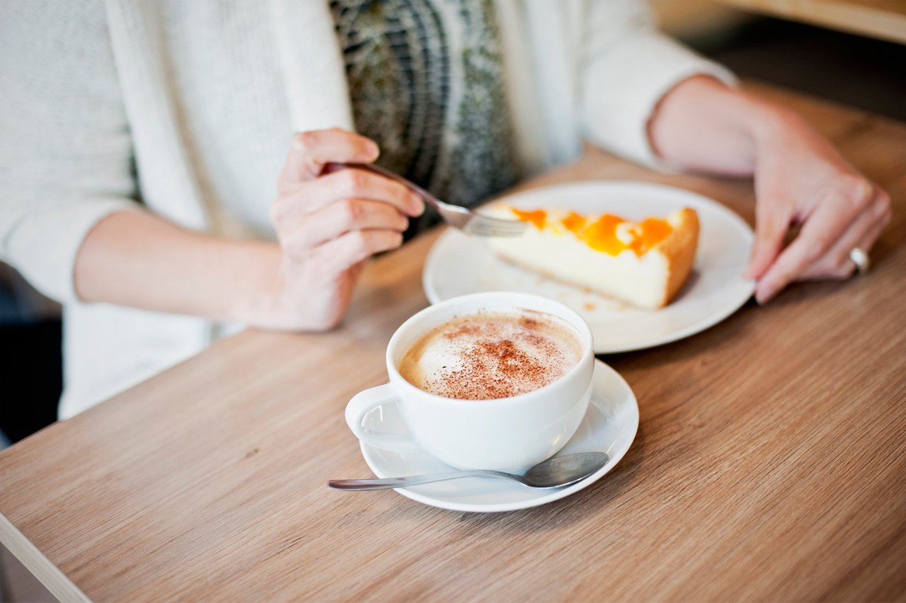 Kaffee und Kuchen weibliche Hand haelt Gabel am Tisch sitzend 