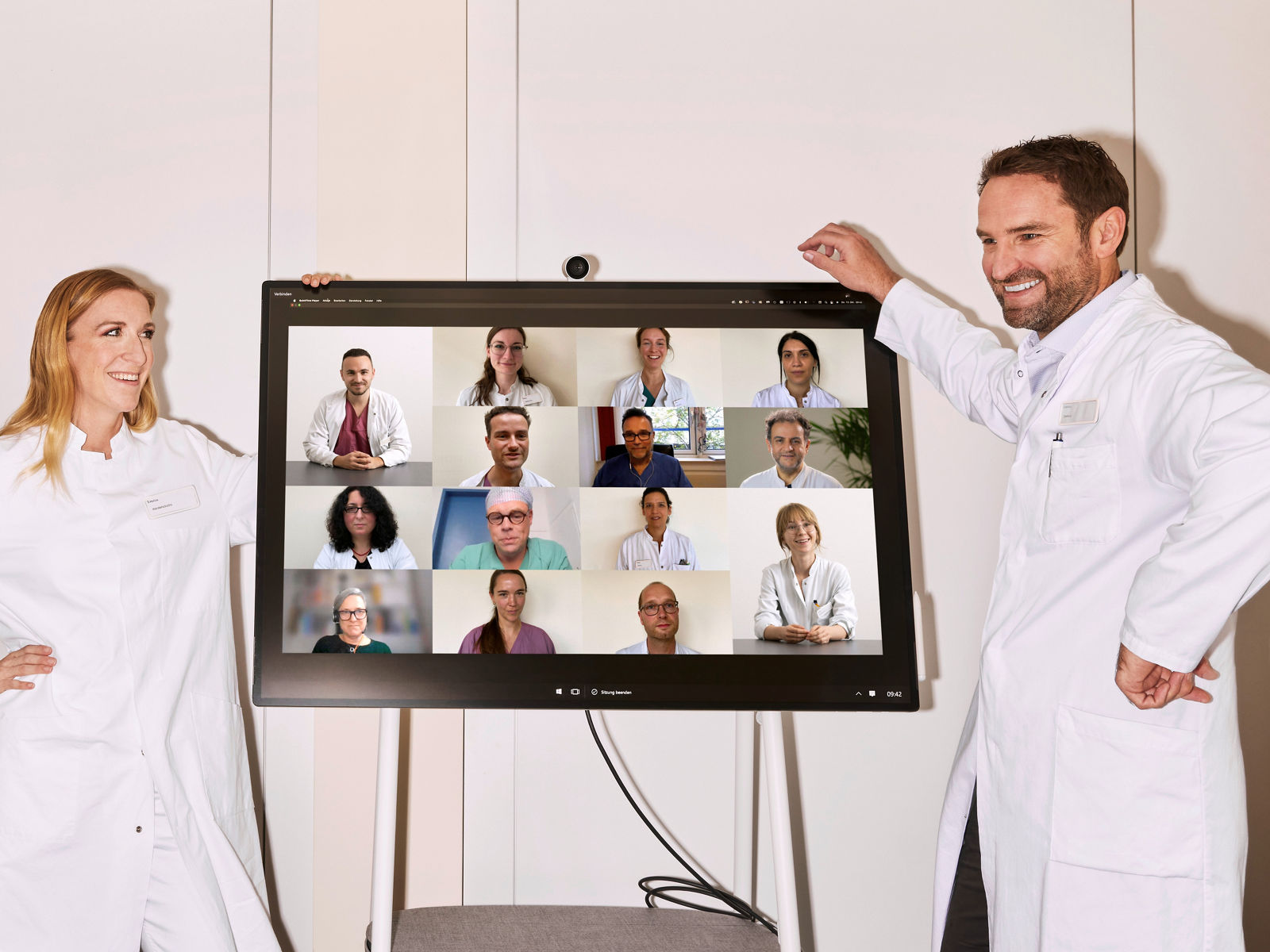 Ärzte in Weiterbildung stehen neben Monitor im Videochat mit weiteren Ärzt:innen #EchtesLeben 2022/23