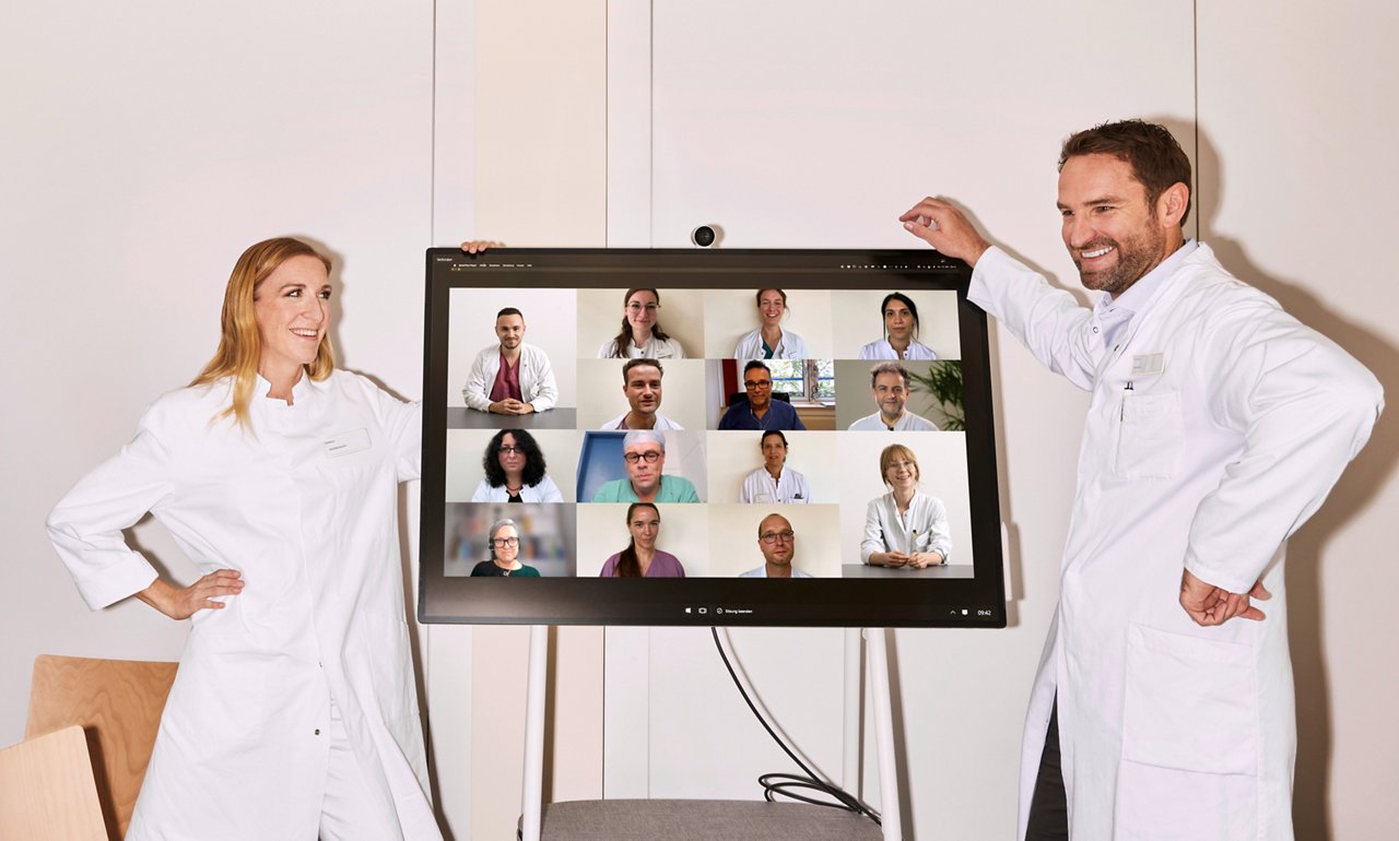 Ärzte in Weiterbildung stehen neben Monitor im Videochat mit weiteren Ärzt:innen #EchtesLeben 2022/23