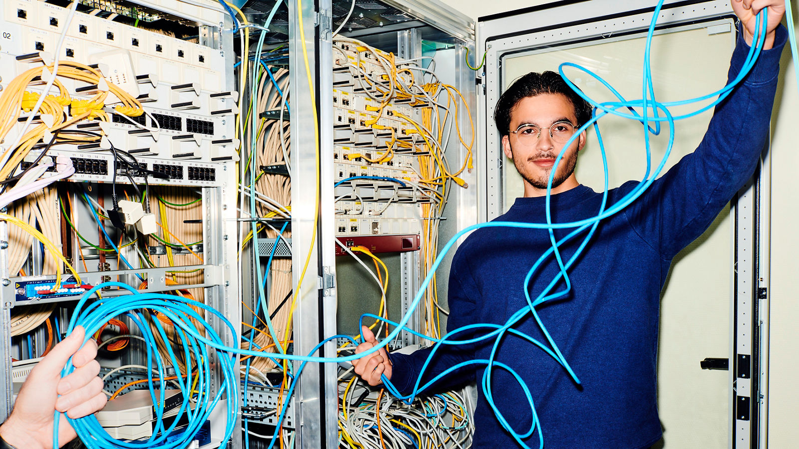 Mitarbeiter steht am Serverschrank und hält ein Kabel in der Hand
