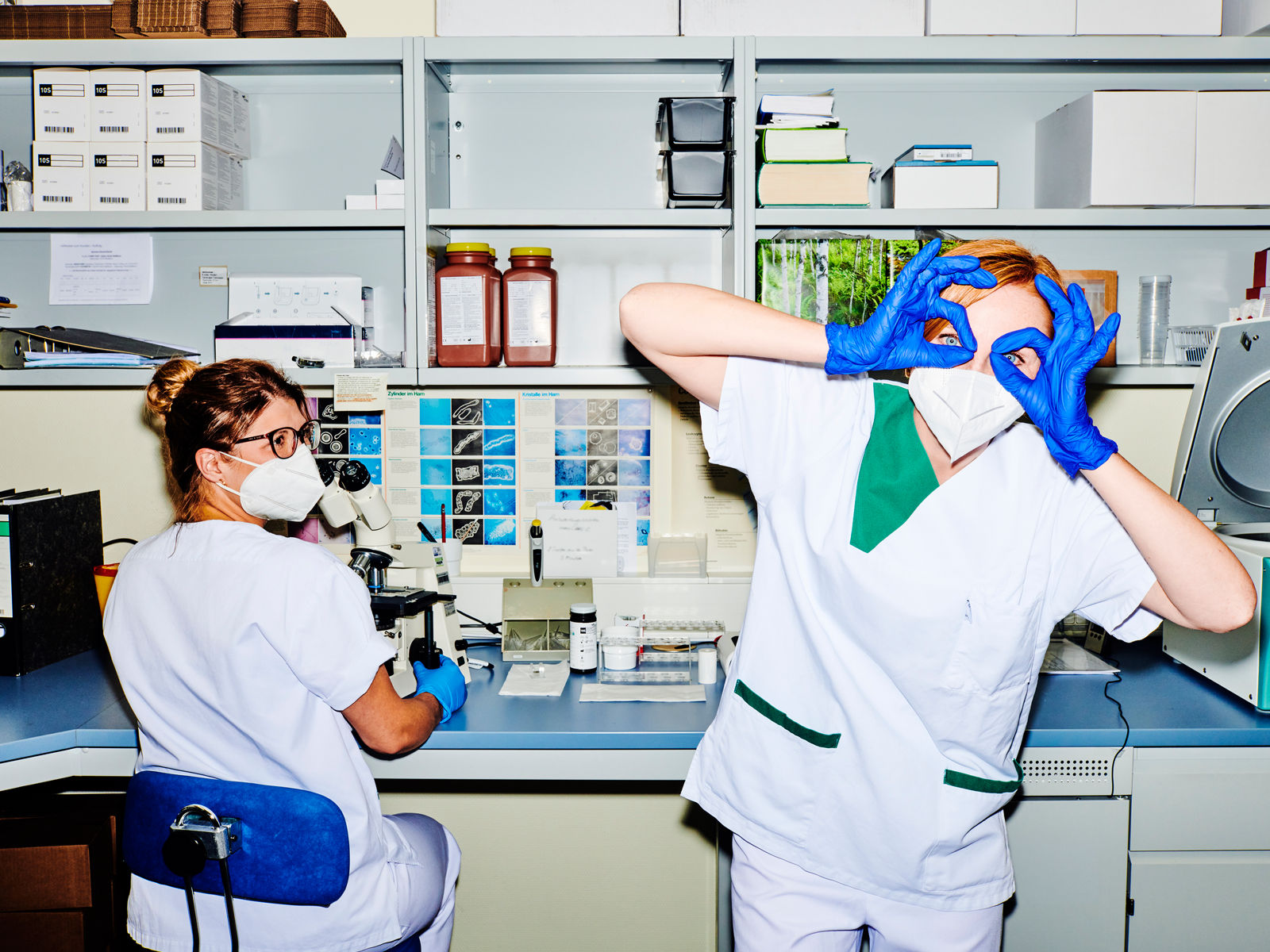 Zwei Mitarbeitende im Labor, eine Mitarbeiterin blickt in die Kamera und hält sich die Hände vors Gesicht als wäre es eine Brille #EchtesLeben 2021/22