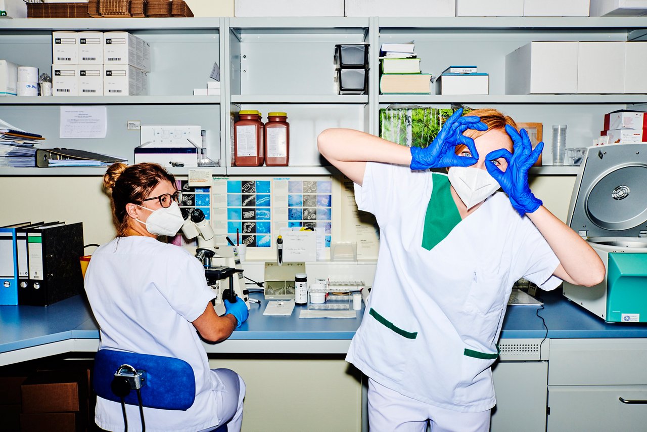 Zwei Mitarbeitende im Labor, eine Mitarbeiterin blickt in die Kamera und hält sich die Hände vors Gesicht als wäre es eine Brille #EchtesLeben 2021/22