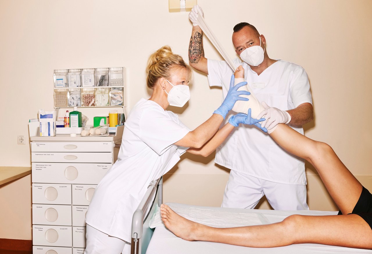 Pflegefach-Team bandagiert den hoch gelegten Fuß eines Patienten #EchtesLeben 2022/23