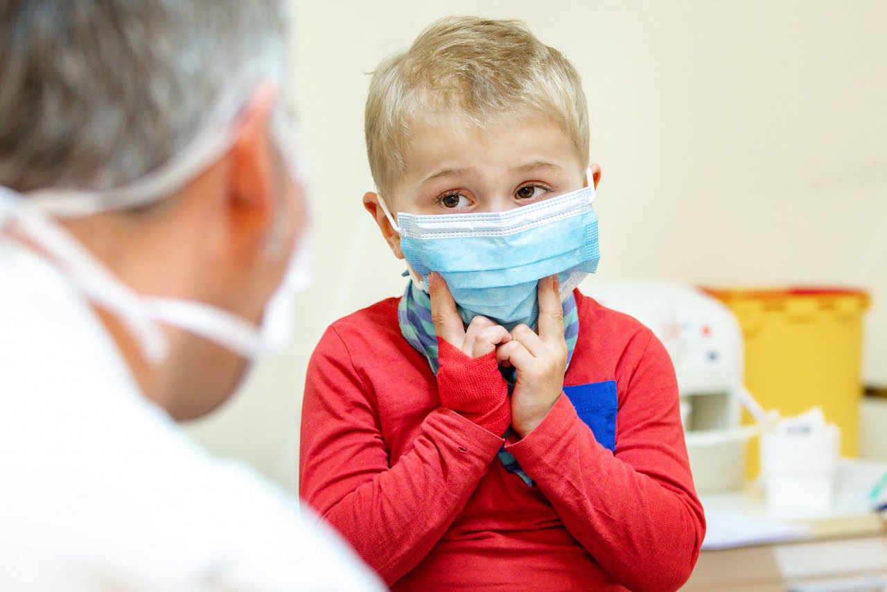 Junge sitzt vor Arzt mit Mundschutz 
