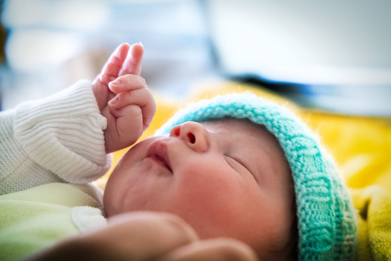 Neugeborenes mit Strickmütze hebt neugierig die Hand.