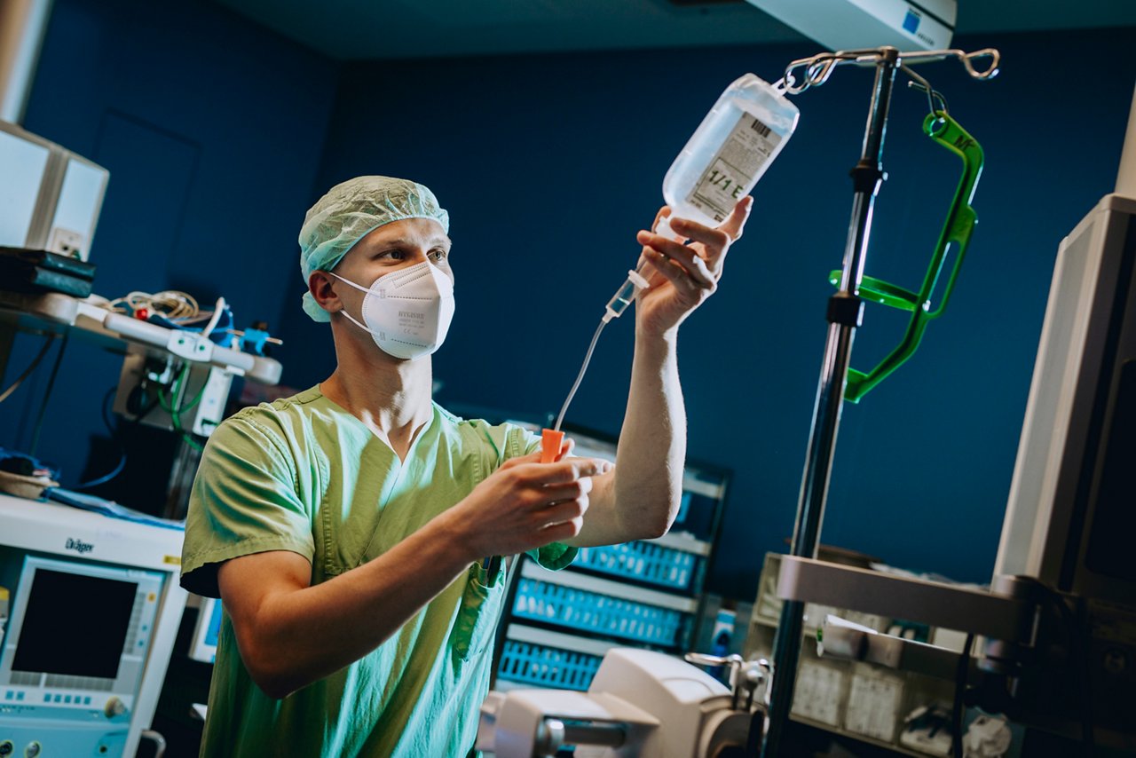 ATA Anaesthesie-Pflege bereitet Infusion vor mit OP-Haube und FFP2-Maske