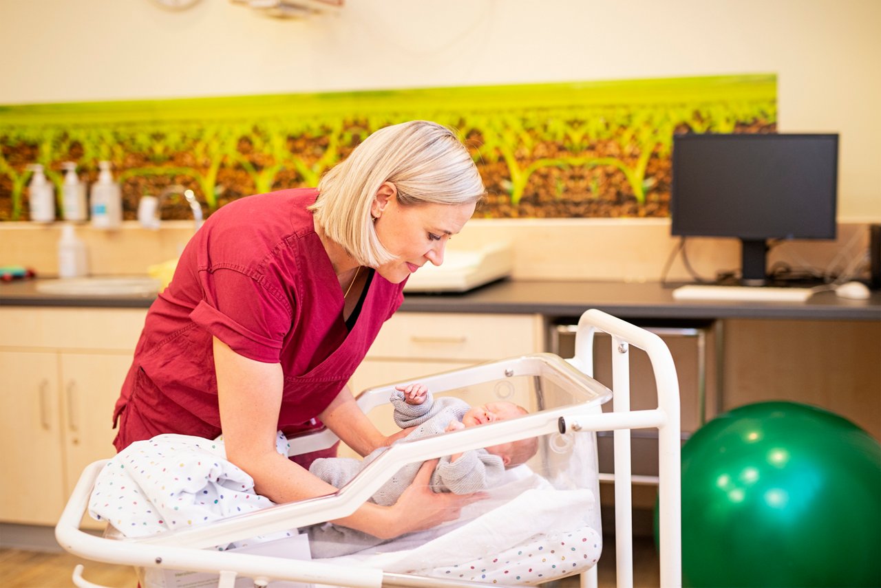 Hebamme legt das Neugeborene ins Babybett