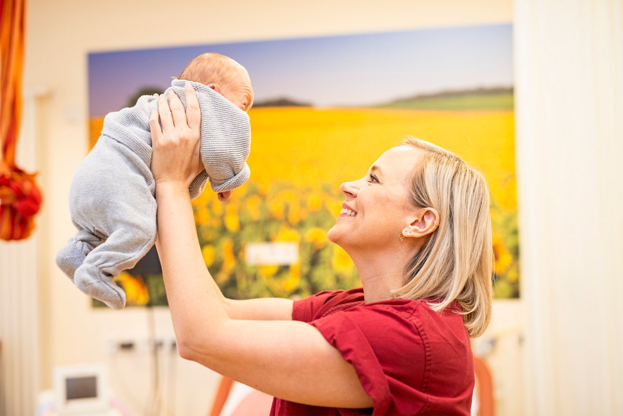 Lächelnde Hebamme hält ein Neugeborenes in den Händen