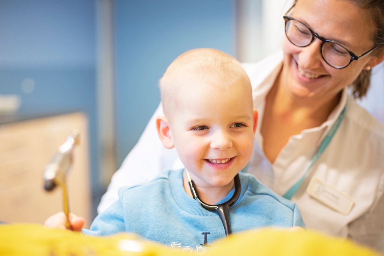 Kleiner onkologischer Patient lachend auf dem Schoß einer Ärztin