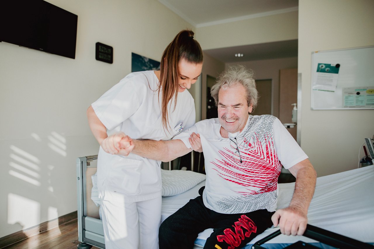 Pflegekraft unterstützt einen Patienten beim Aufstehen