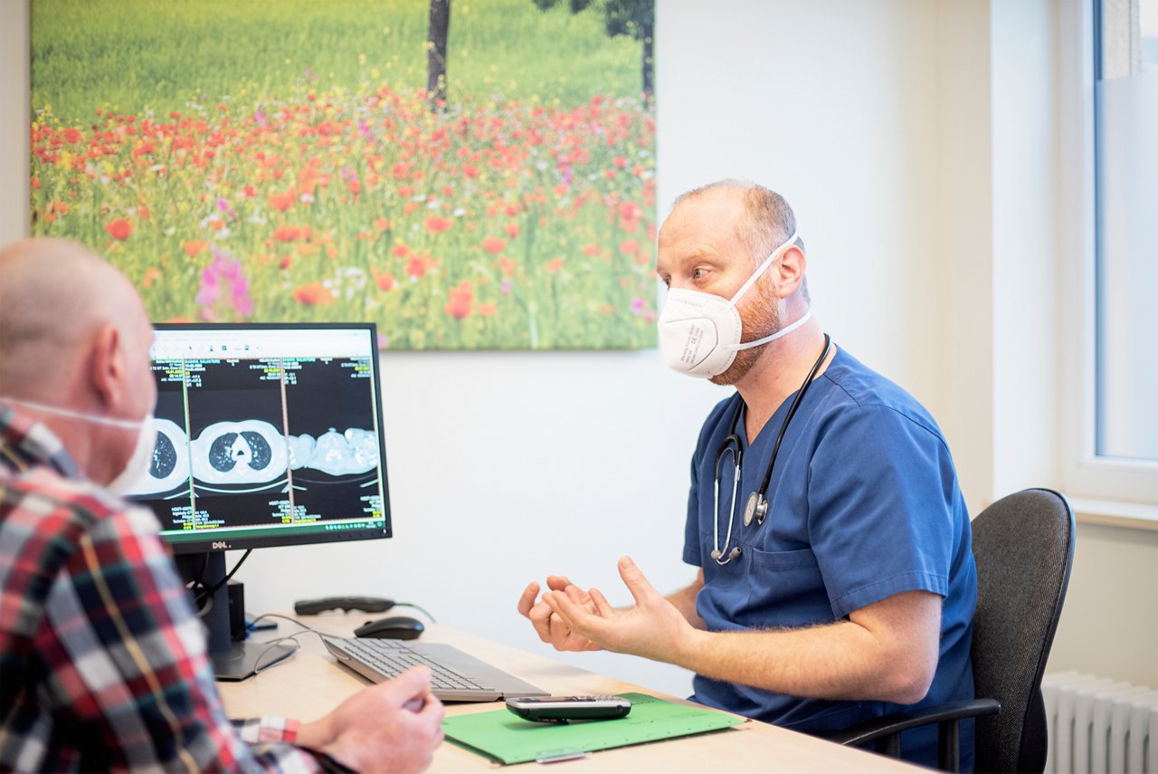 Lungenfacharzt Benoit Krämer im Gespräch mit einem Patienten am Schreibtisch, PC zeigt ein Röntgenbild der Lunge. 