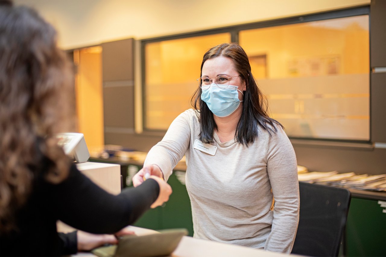 Mitarbeiterin in der Zentralambulanz begrüßt Patientin