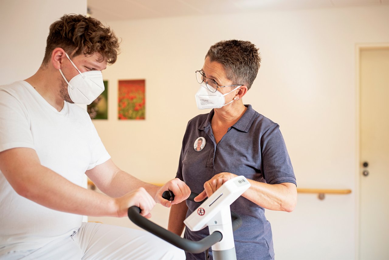 Physiotherapeutin unterstützt Krebspatient am Trainingsgerät