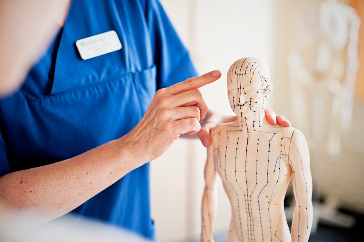 Chefärztin stellt die Schmerzbehandlung auf einer Schmerztherapie-Puppe dar.