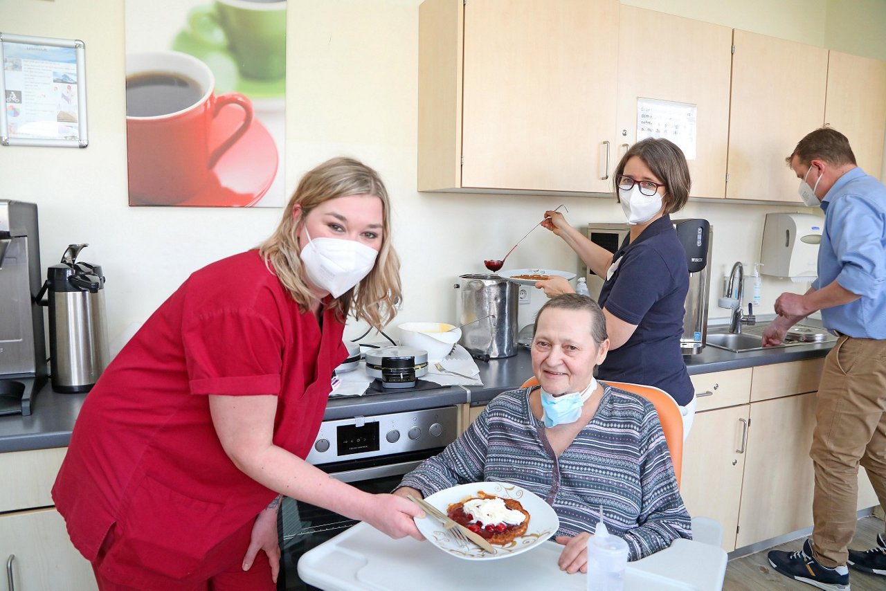 Stationsleitung gibt einer Patientin im Rollstuhl eine Waffel in der Küche auf der Station Lebensluft  in Krefeld.