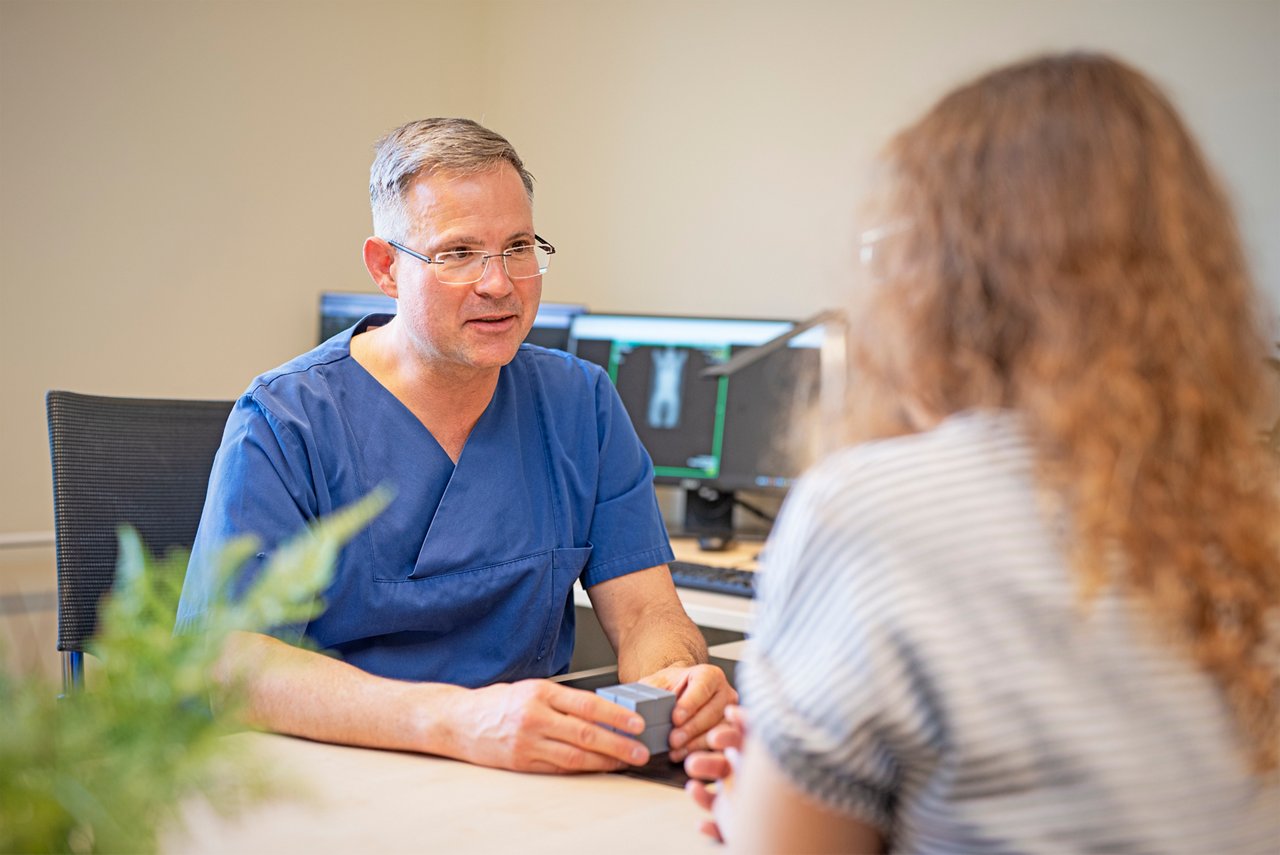 Chefarzt Dr. Daum-Marzian führt am Schreibtisch sitzend ein Gespräch mit einer Patientin 
