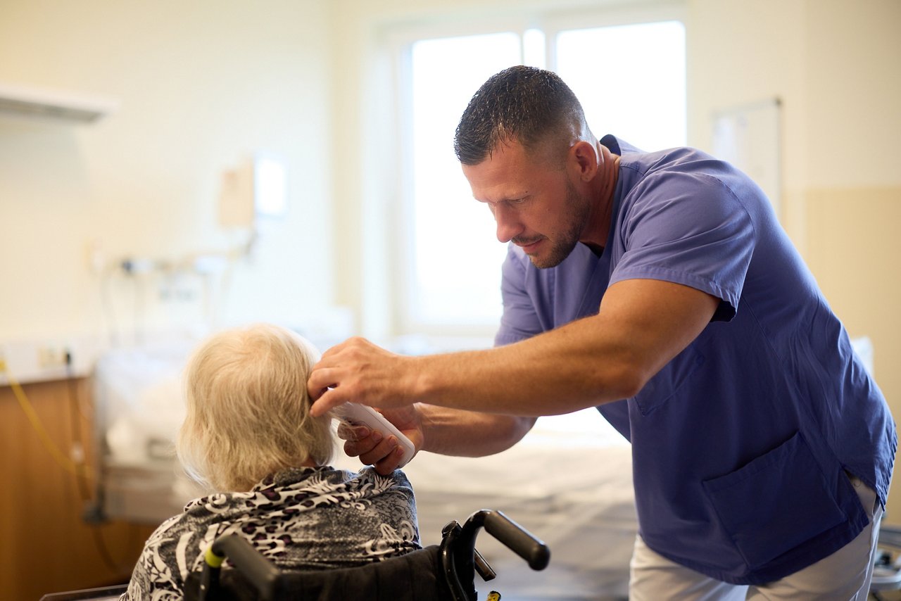 Pfleger misst bei einer Patientin die Körpertemperatur mit einem Ohrthermometer