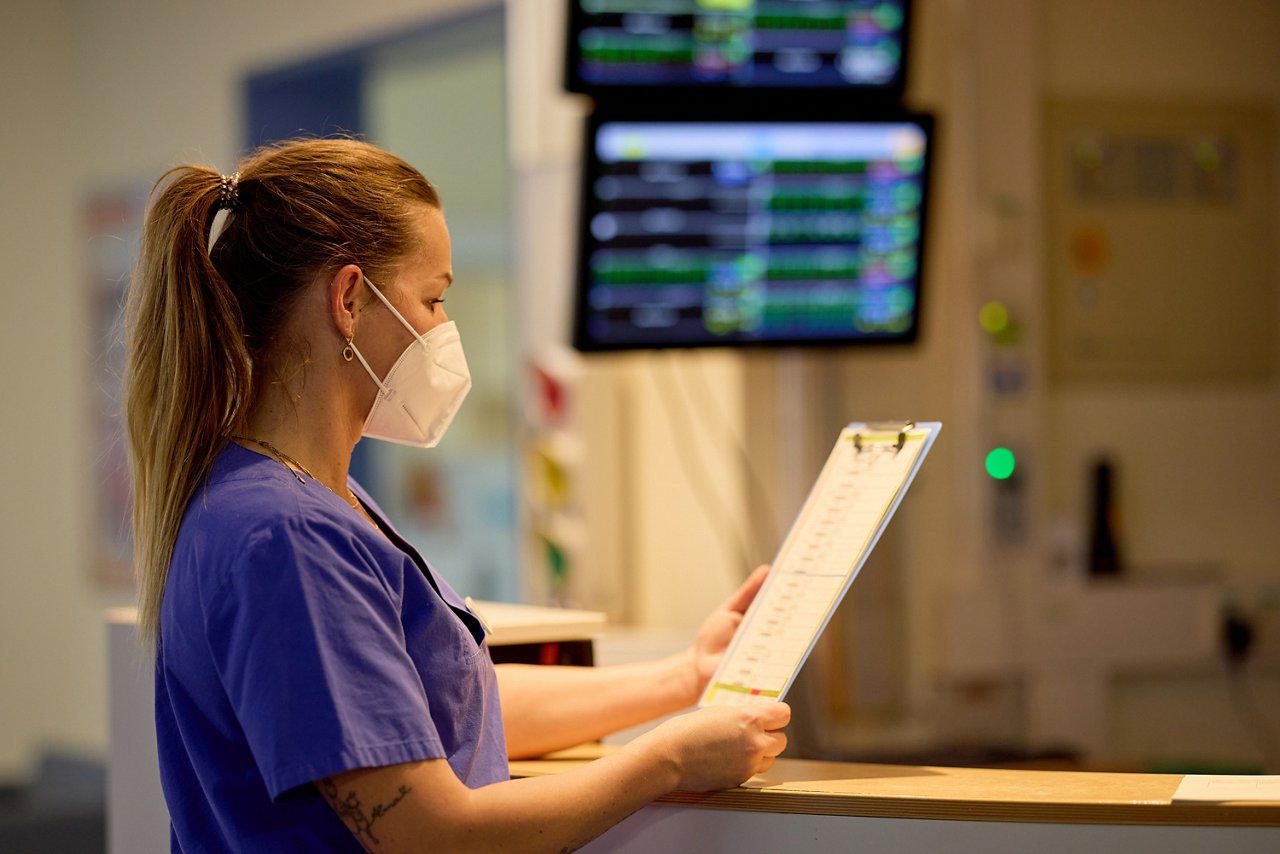 Pflegefachfrau steht vor Monitoren und blickt auf eine Patientenkurve