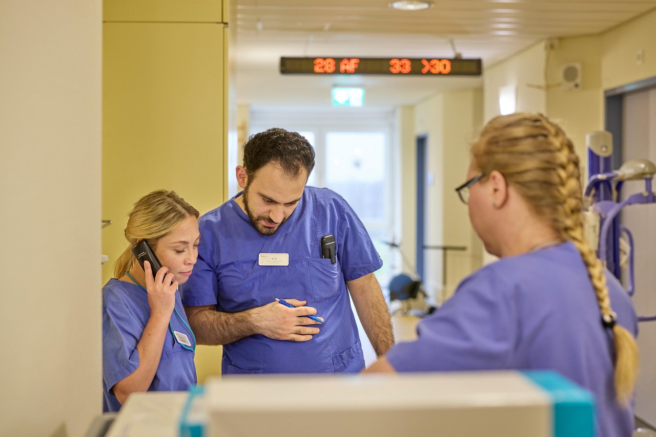 Pflegerinnen und Arzt besprechen eine Behandlung auf dem Stationsflur