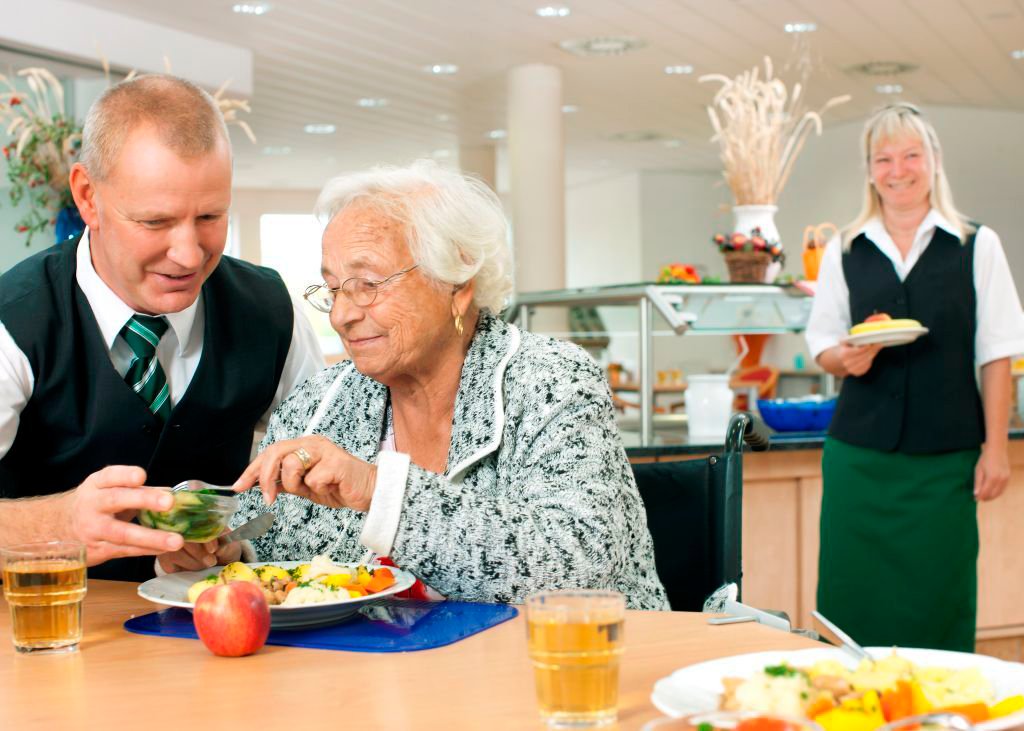Servicemitarbeiter hilft Patientin beim Essen