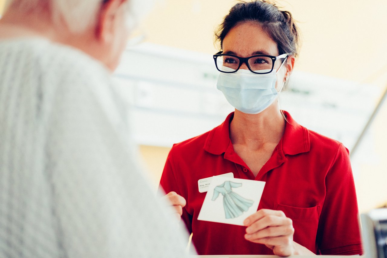 Logopädin hält dem Patienten eine Karte hin auf dem ein Kleid abgebildet ist