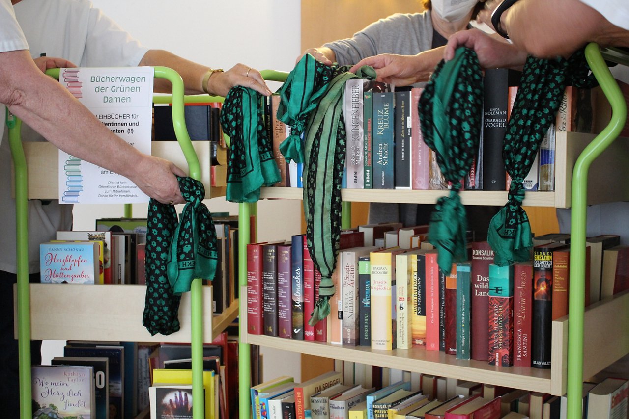 Hände halten vor einem Bücherwagen ein grünes Tuch.
