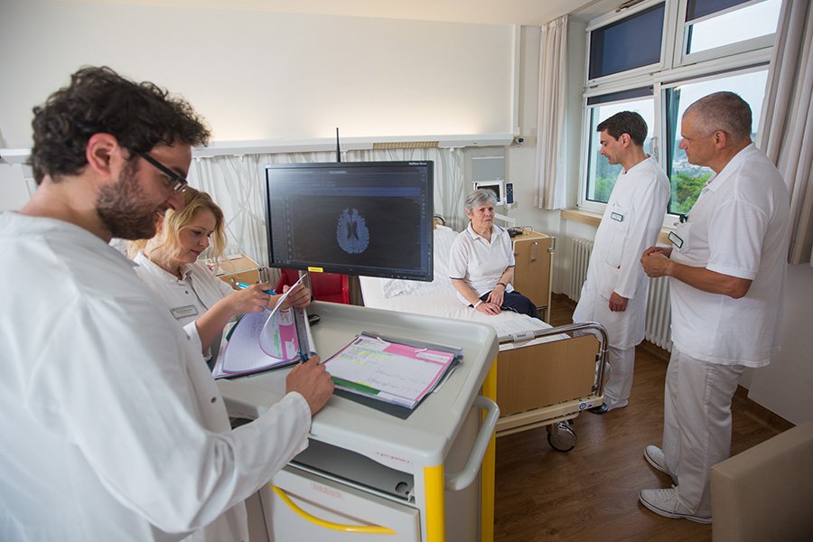 Pfleger und Ärzte stehen im Patientenzimmer und klären den Patienten auf