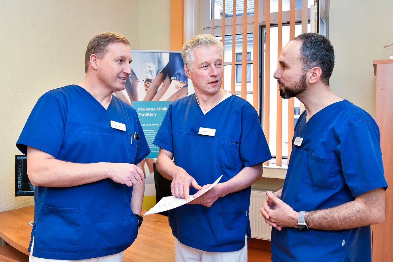 Drei Ärzte der Unfallchirurgie besprechen Dokument in der Hand