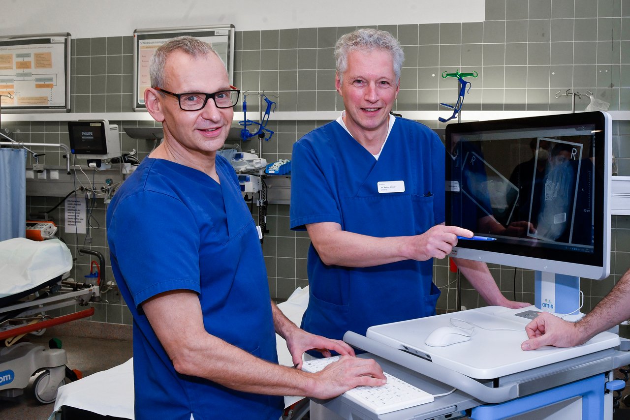 Zwei Ärzte der Unfallchirurgie stehen am Visitenwagen im Schockraum und erklären Röntgenbilder. 