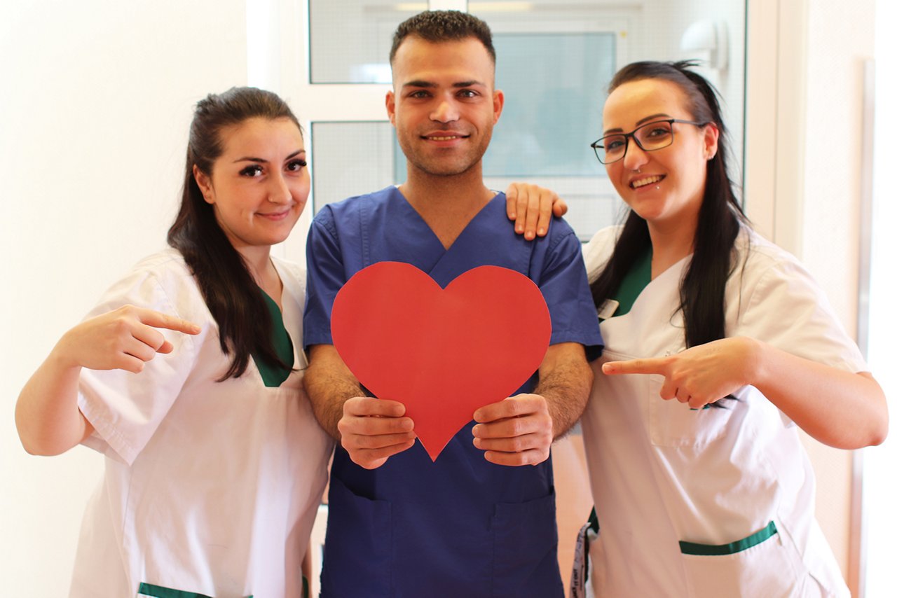 Drei Pflegekräfte zeigen auf rotes Herz in der Hand zu Valentinstag