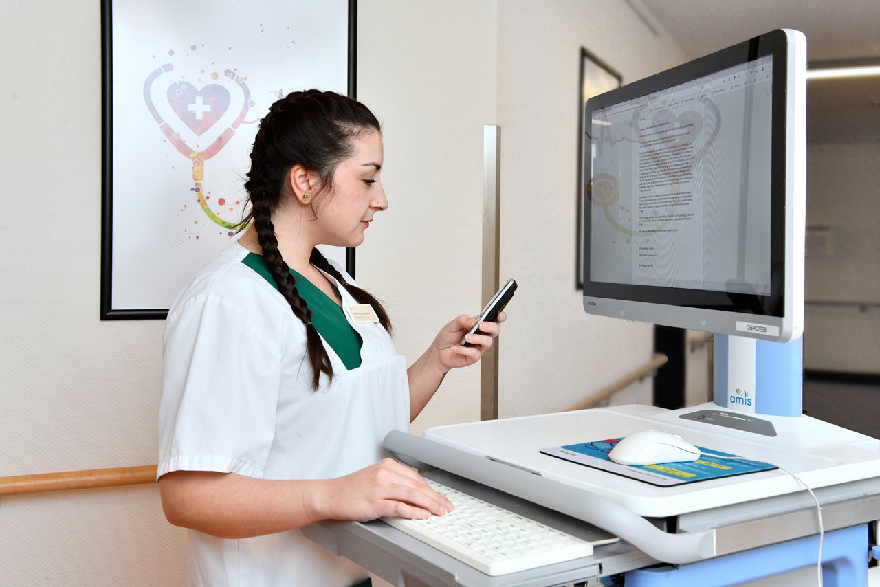 Pflegekraft am mobilen Visitenwagen auf Flur mit Patientenakten