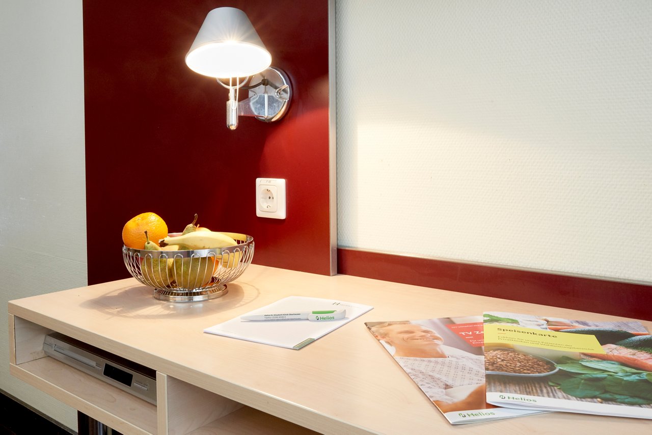 Schreibtisch der Privatklinik mit Speisekarte, Notizblock und Obstkorb