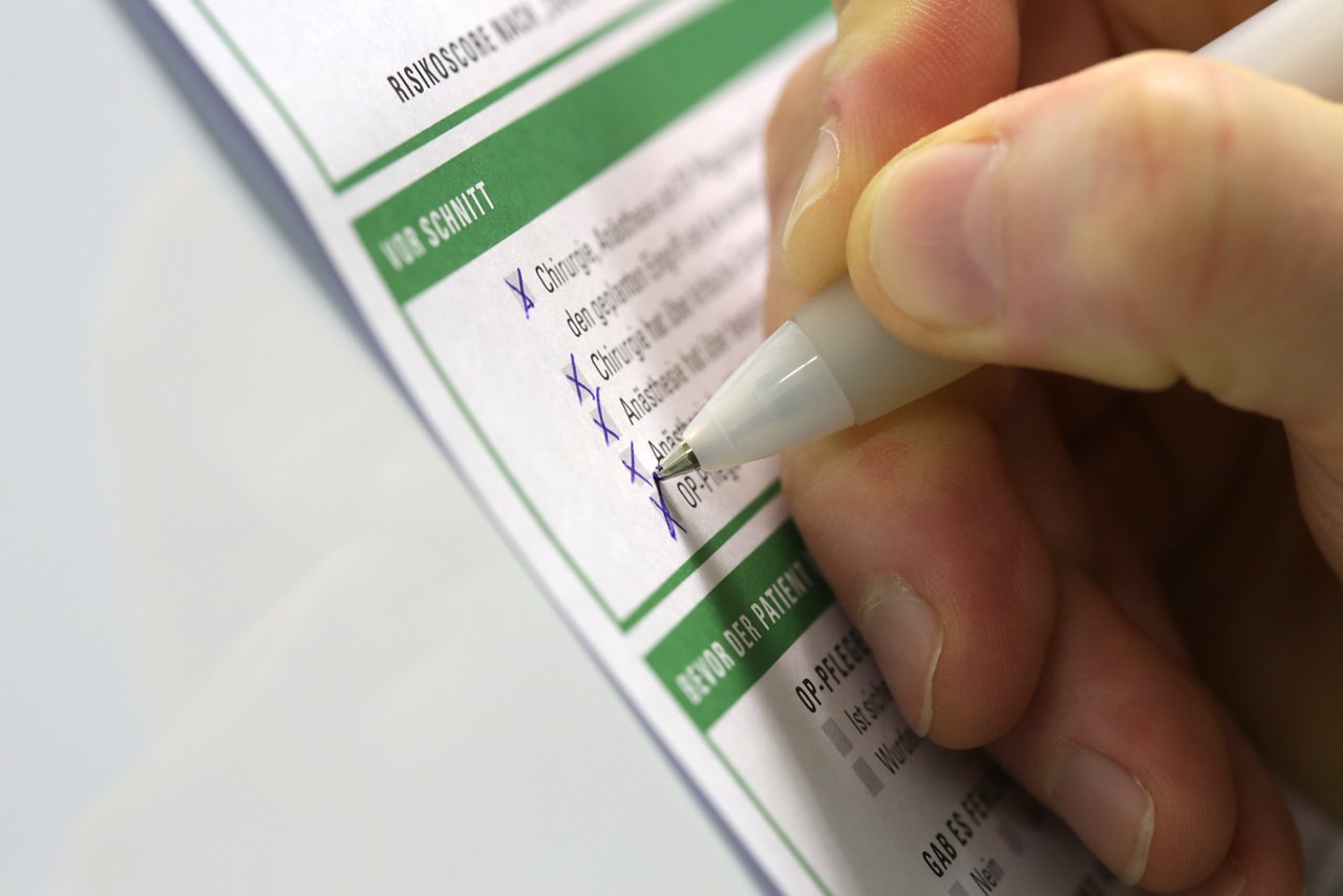 Hand die mit einem Kugelschreiber Kreuze auf einer OP-Checkliste setzt