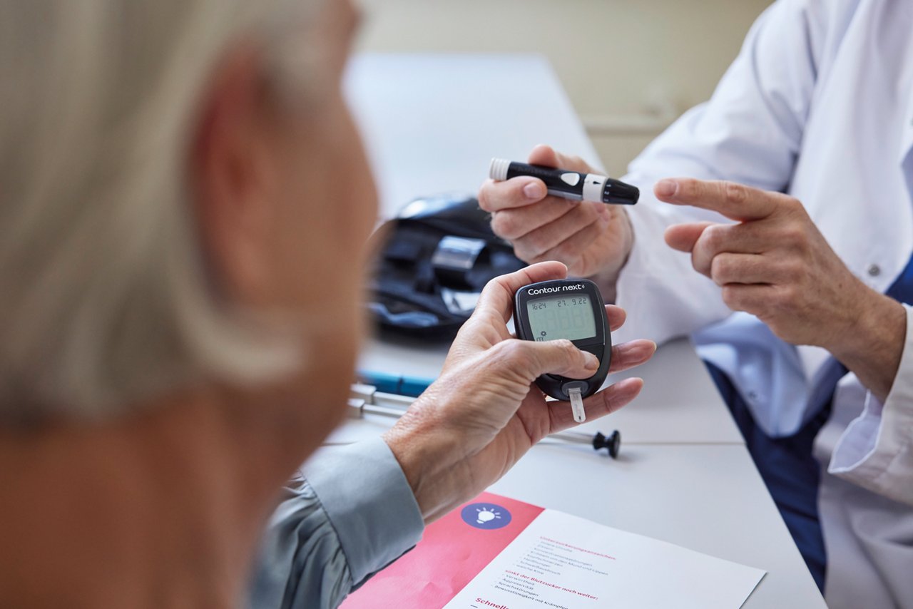Arzt erklärt Patientin, wie man ein Messgerät zur Messung des Blutzuckerspiegels richtig verwendet