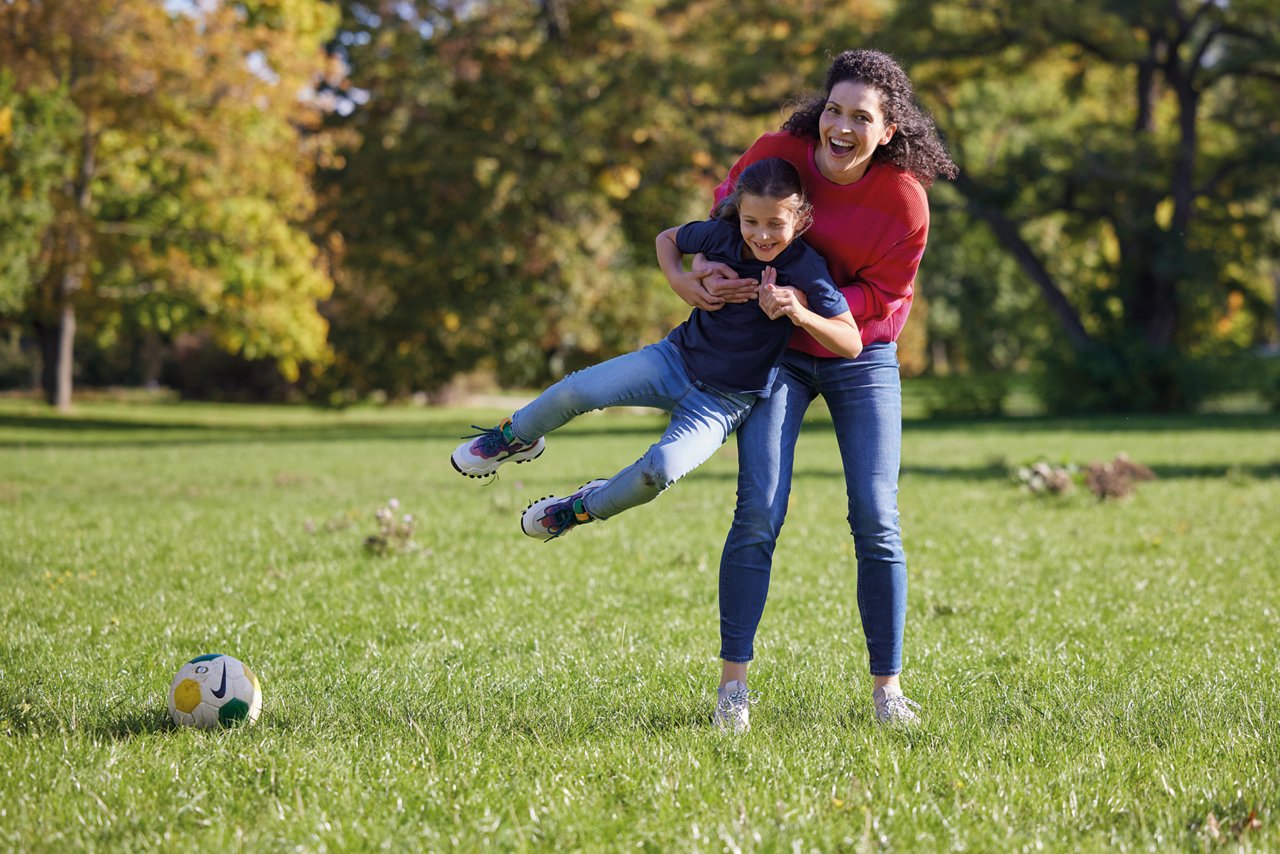 Mutter und Kind toben im Park und spielen Fußball