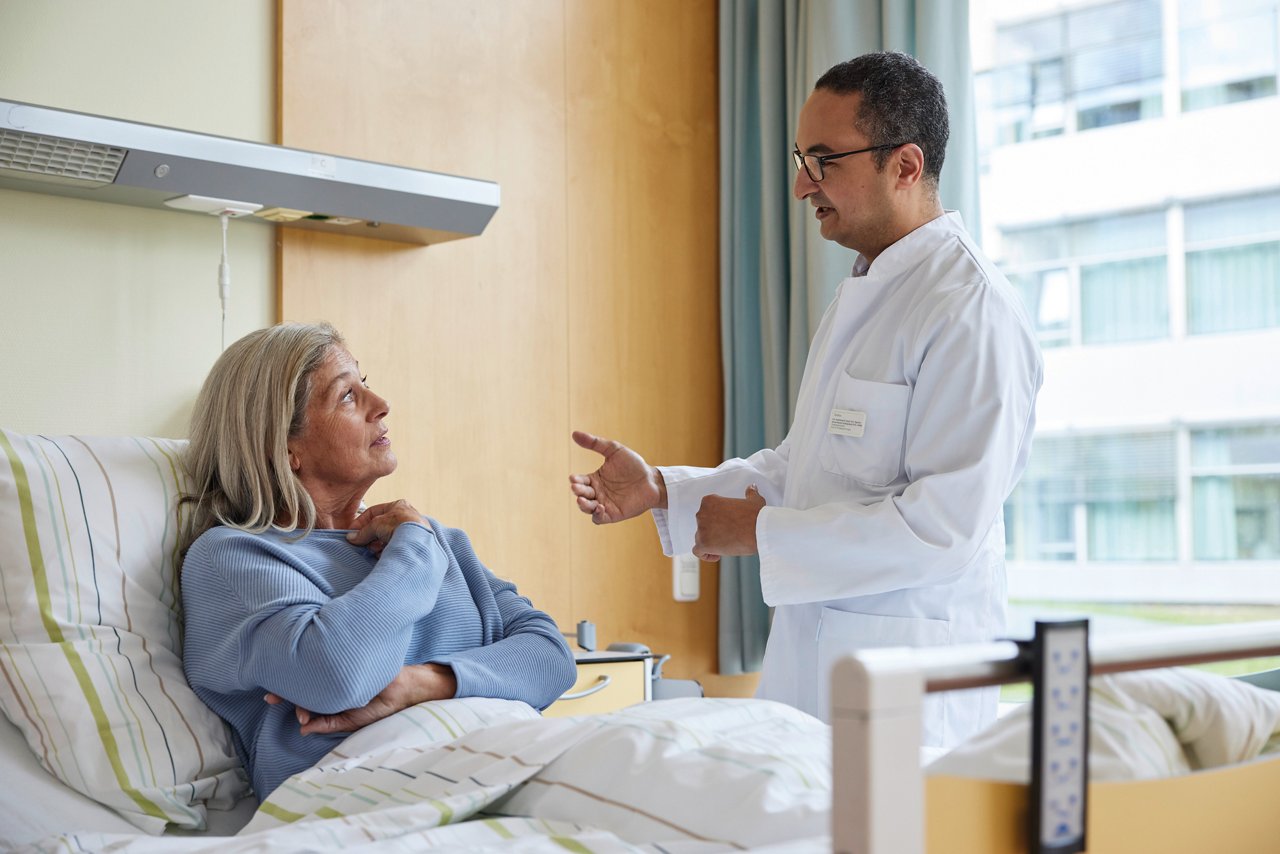 Orthopäde im Gespräch mit Patientin im Bett in einem Patientenzimmer