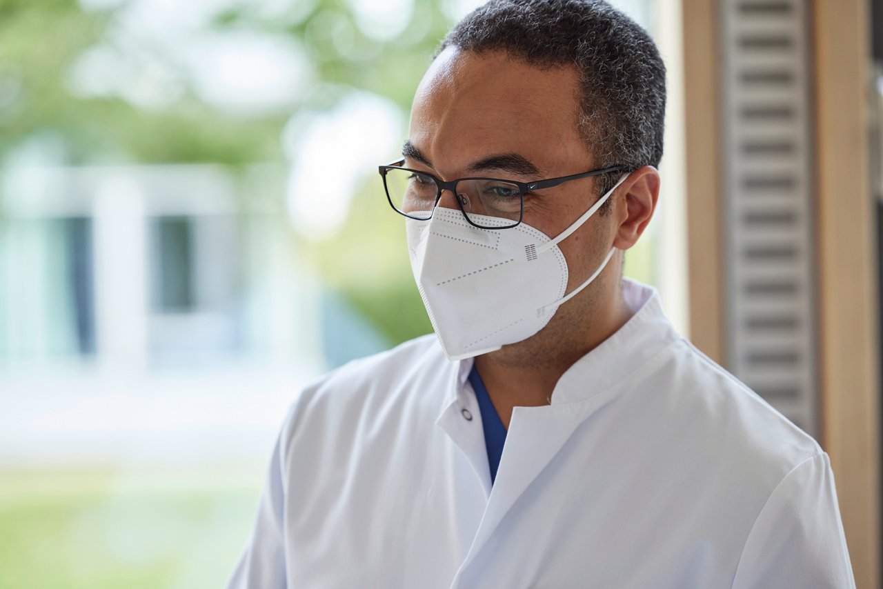 Orthopäde mit Maske und Brille und freundlichem Blick