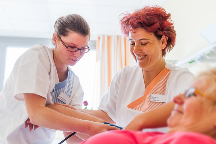 Auszubildende unter Anleitung einer Krankenschwester misst Blutdruck an Patientin