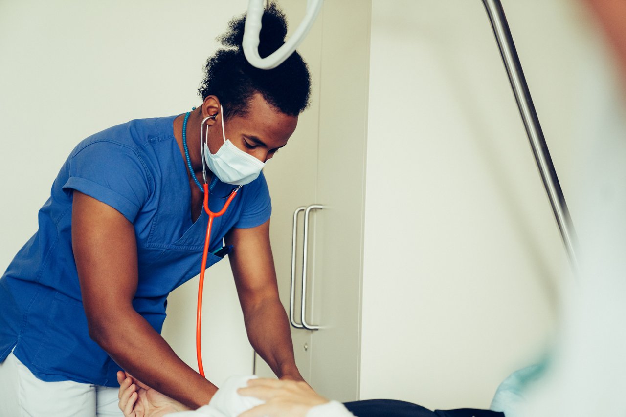 Pfleger mit Stethoskop bei der Untersuchung am Krankenbett
