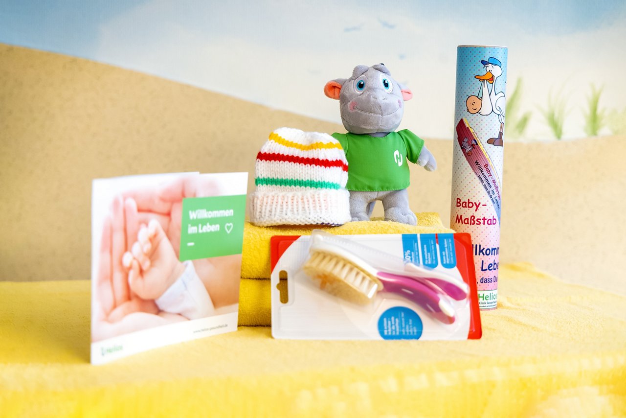 Liebevolle Kleinigkeiten wie Babymütze, Stofftier und Maßband als kleine Geschenke für Mütter nach der Geburt