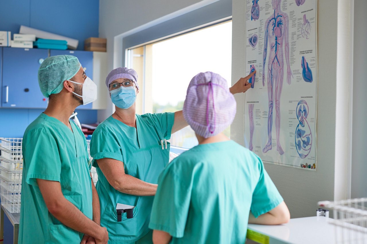 Praxisanleiterin erklärt Auszubildenden die menschliche Anatomie vor einem Fachplakat