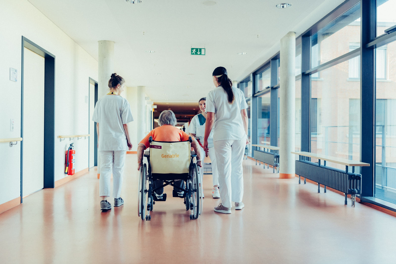 Drei Pflegerinnen und eine Patientin im Rollstuhl auf einem hellen Flur