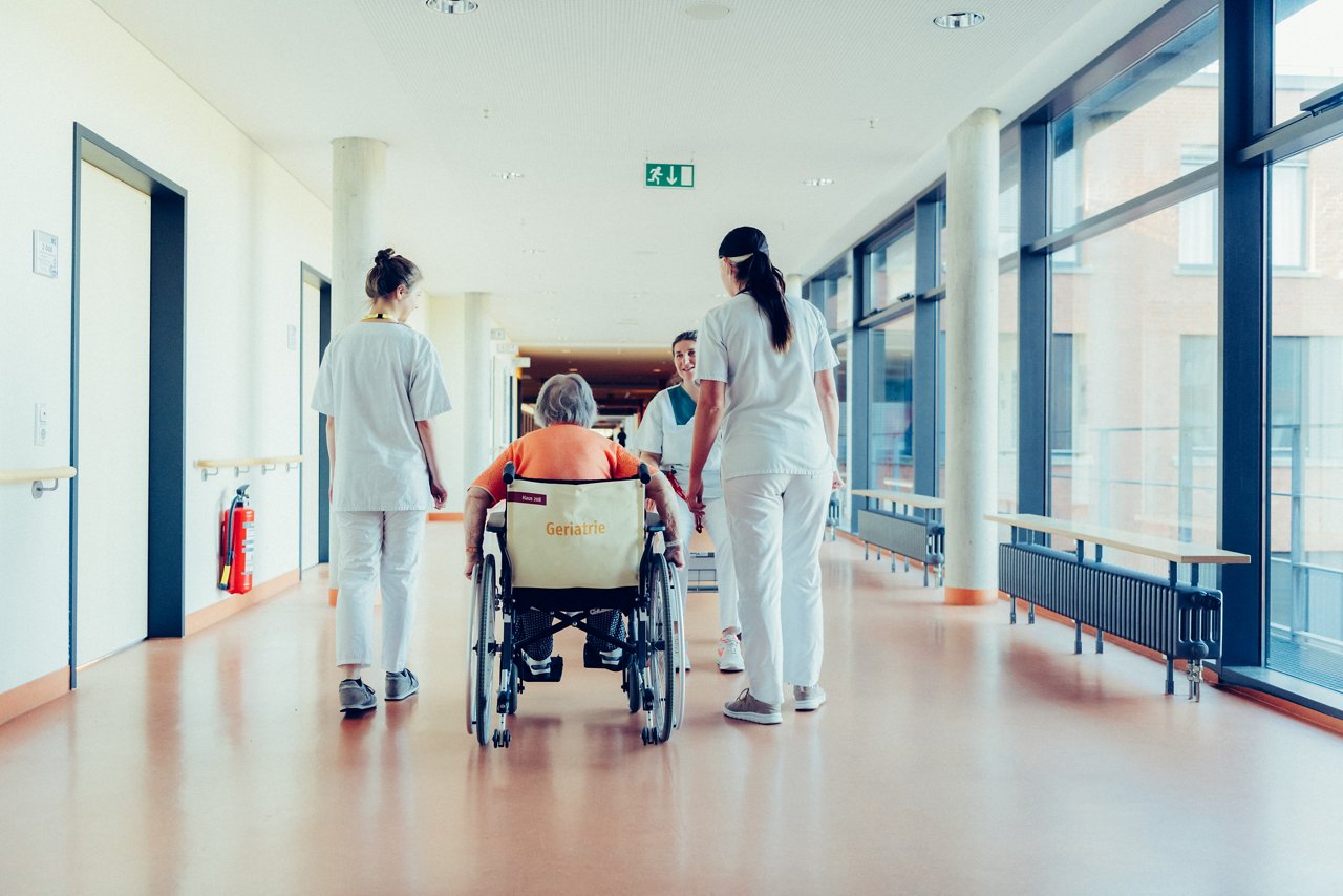 Drei Pflegerinnen und eine Patientin im Rollstuhl auf einem hellen Flur